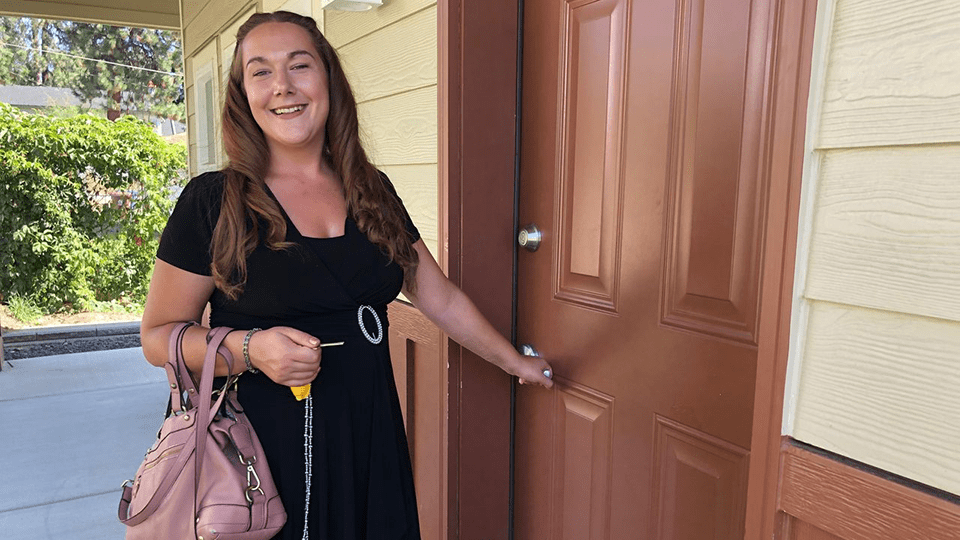smiling woman holding house key in her hand while other hand turning door knob