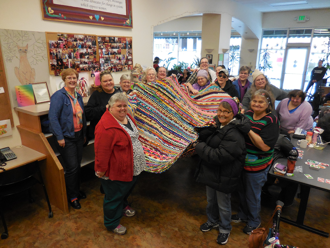 group of women holding up crocheted blanket