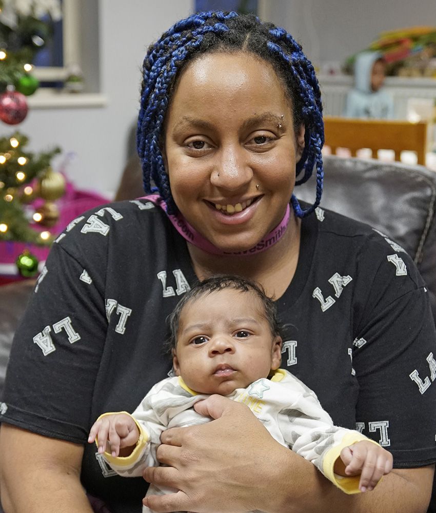 smiling black mom holding baby in front of christmas tree